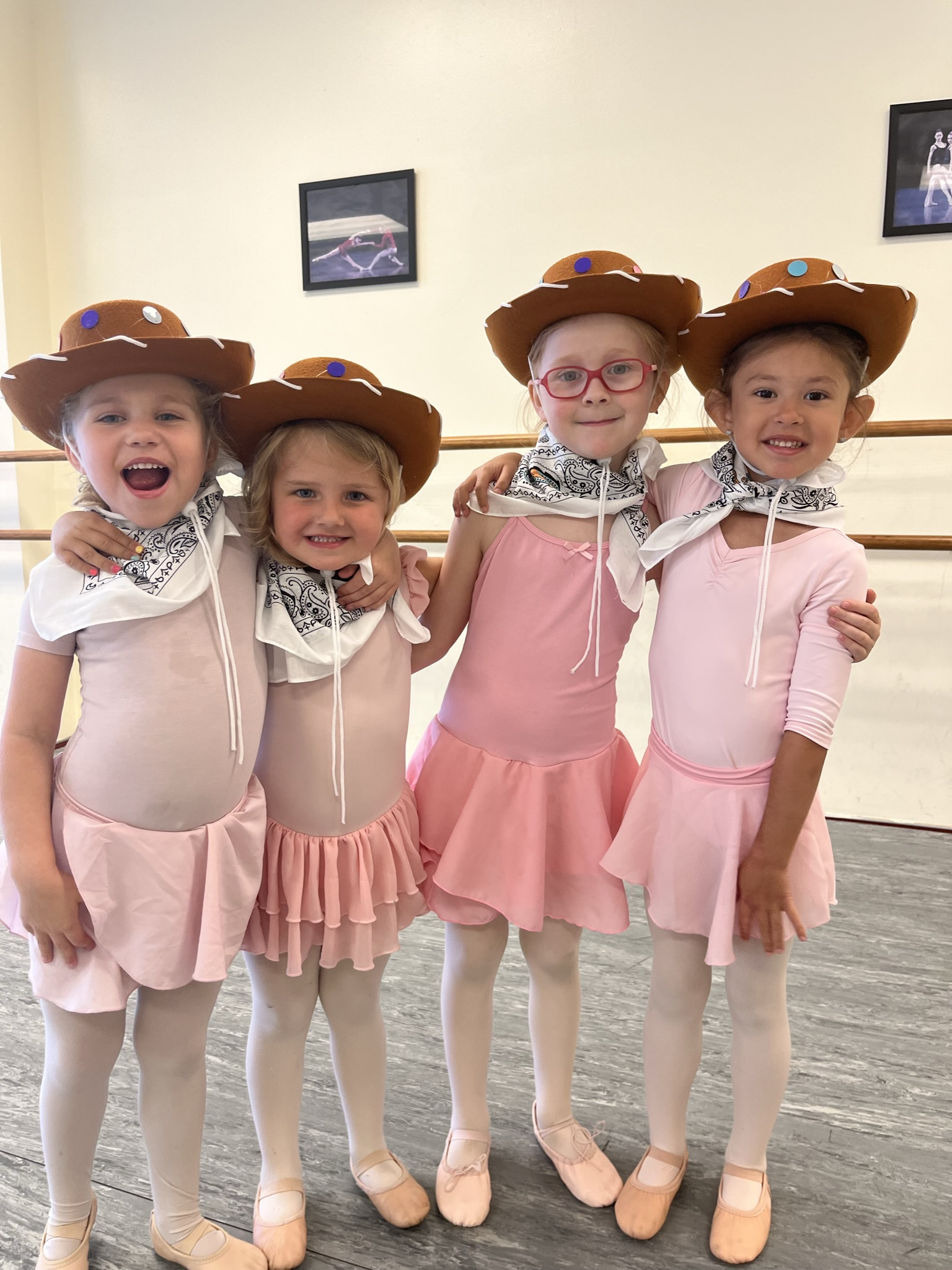 Group of young girls with arms around each other in pink leotards and cowboy hats